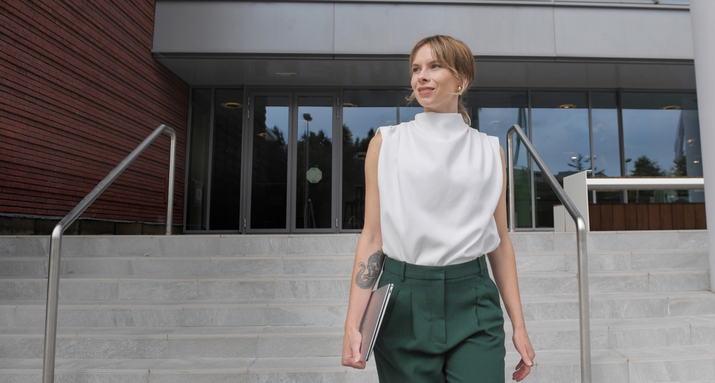A woman carrying a laptop walks down the steps of an office building