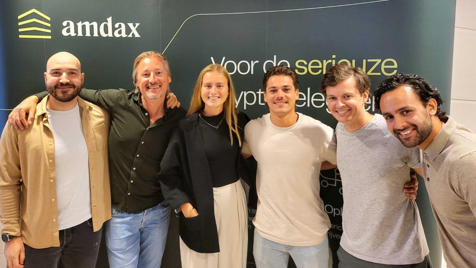 Group photo of six smiling Amdax colleagues in front of an Amdax banner